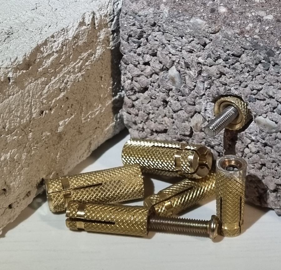 Boccole BLOWLOCK in ottone per muratura accanto a campioni di intonaco e calcestruzzo